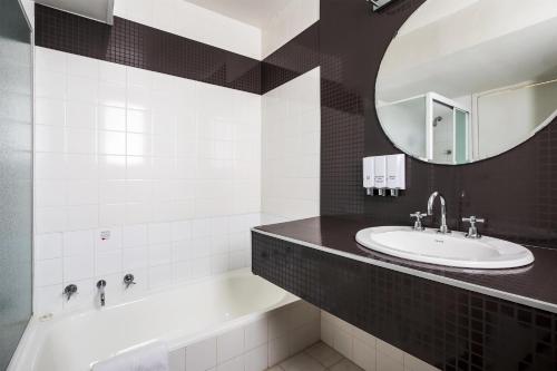 a bathroom with a sink and a tub and a mirror at Metro Hotel Perth in Perth