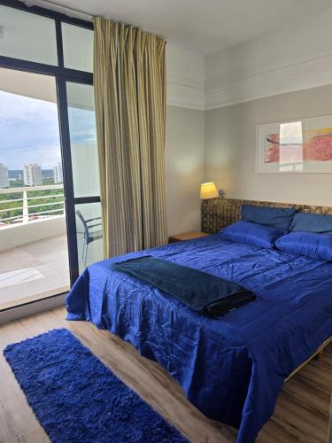 a bedroom with a blue bed and a large window at Suíte com varanda Tropical Hotel in Manaus