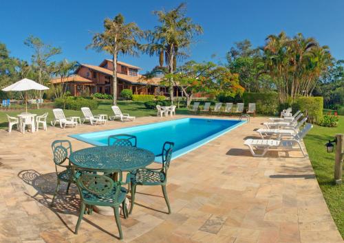 a pool with tables and chairs next to a house at Hotel Pousada da Lagoa in Garopaba