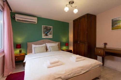 a bedroom with a large white bed with a green wall at Aleko Apartments City Center in Veliko Tŭrnovo