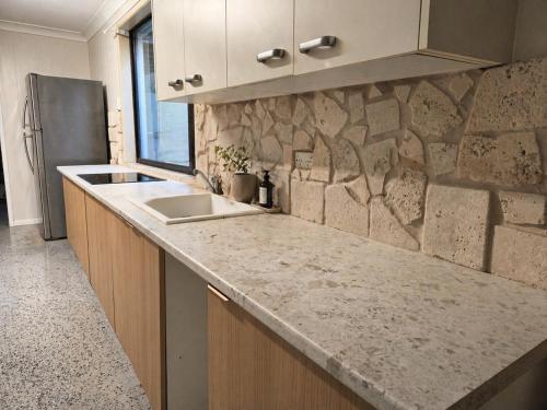 a kitchen with a sink and a stone wall at Kookaburra Guesthouse in Coffs Harbour