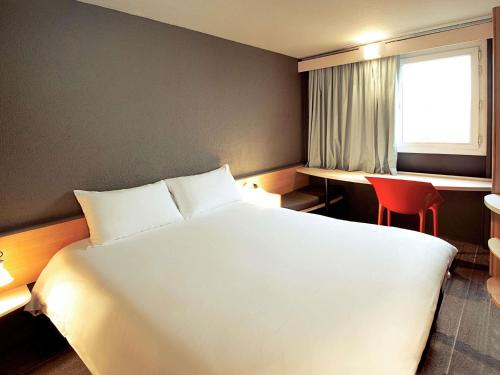 a bedroom with a large white bed and a red chair at IBIS Fourmies in Fourmies