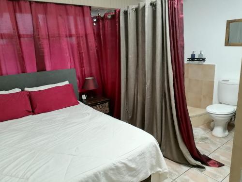 a bedroom with a bed with red curtains and a toilet at Reizigers Rusten in Kempton Park