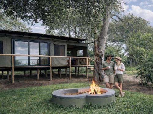 two people standing next to a fire pit in the grass at Buffalo Tented Camps in Mahango