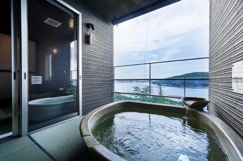 a bathroom with a tub with a view of the water at Kisara Bettei TOKI in Toba