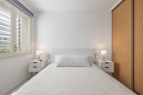 a white bedroom with a large bed and two night stands at Resguardo en la playa in Calafell