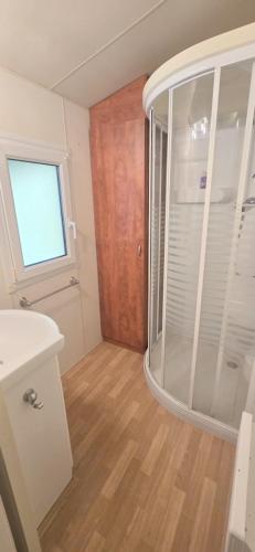a bathroom with a glass shower and a wooden floor at Bungalow-Mobilhome - Petit prix- Océan -Forêt -Camping 3 étoiles in Bias