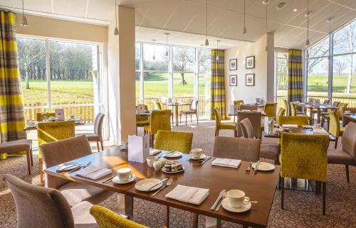 uma sala de jantar com mesas, cadeiras e janelas em Sandford Springs Hotel and Golf Club em Kingsclere