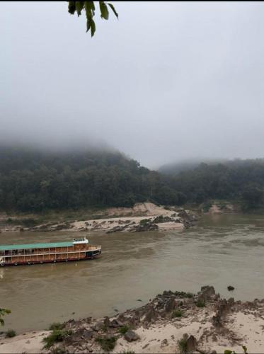 a boat on a river with a mountain in the background at Janh Ya Phone Guesthouse in Pakbeng