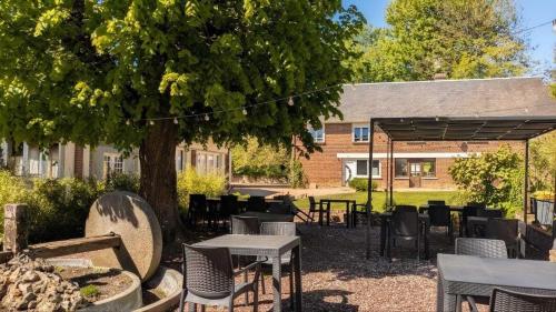 a patio with tables and chairs under a tree at L'Authentique in Beaumont-le-Roger