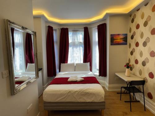a bedroom with a bed with red curtains and a mirror at Lyon House Hotel in Barking