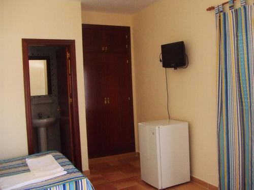 Habitación con nevera pequeña y TV en la pared. en Apartamentos Las Parcelas, en Conil de la Frontera