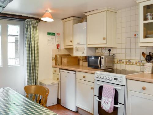 a kitchen with white cabinets and a stove top oven at Yew Tree Cottage in Arford