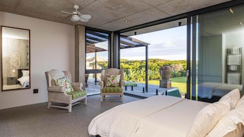 a bedroom with a bed and chairs and a large window at Mi Amor Beach House in Sedgefield