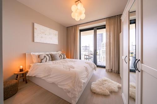 a white bedroom with a bed and a balcony at Top uitzicht luxe appartement DUNES met terras POOL & GYM in Ostend