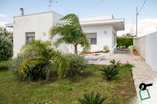 a white house with palm trees in the yard at Hotiday Torre Lapillo Centro in Torre Lapillo