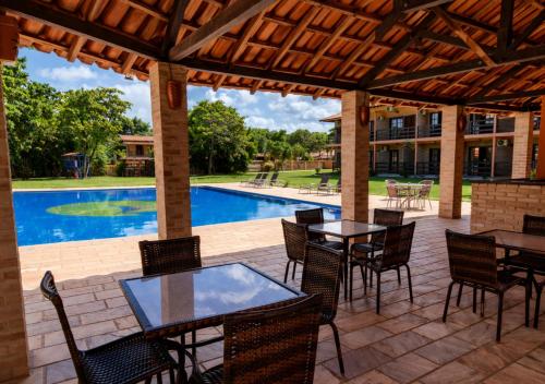 a patio with tables and chairs and a swimming pool at Hotel Cumuruxatiba in Cumuruxatiba