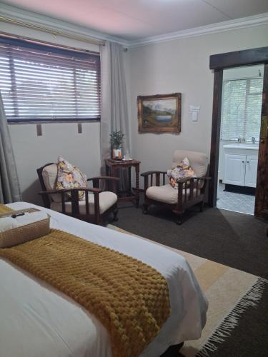 a bedroom with a bed and chairs and a window at Tuscana Villa Guesthouse in Kroonstad