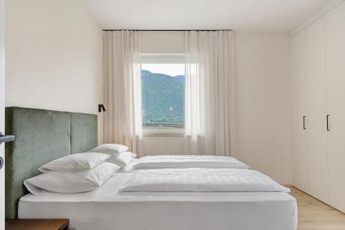 a white bedroom with two beds and a window at Gisshübelhof Apartments in Lana