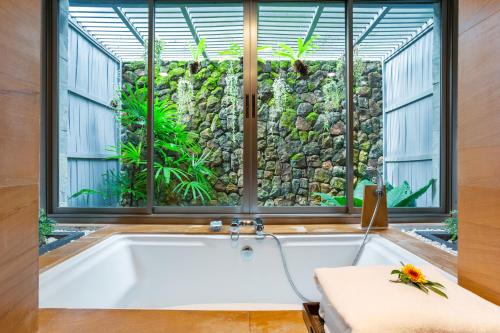 a bath tub in a room with a large window at Nakamanda Resort and Spa in Klong Muang Beach