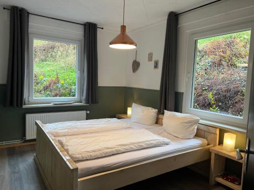 a bed in a room with two windows at Platell Ferienhäuser Harz Lerbach in Lerbach