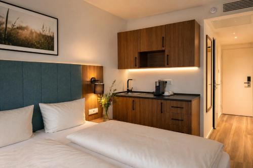 a bedroom with a white bed and a kitchen at Lillys Hotel München in Unterschleißheim
