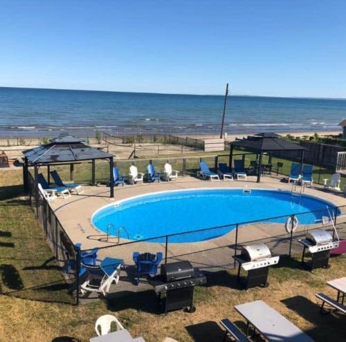 a swimming pool with chairs and umbrellas next to the ocean at Beachy Daze in Wasaga Beach in Wasaga Beach