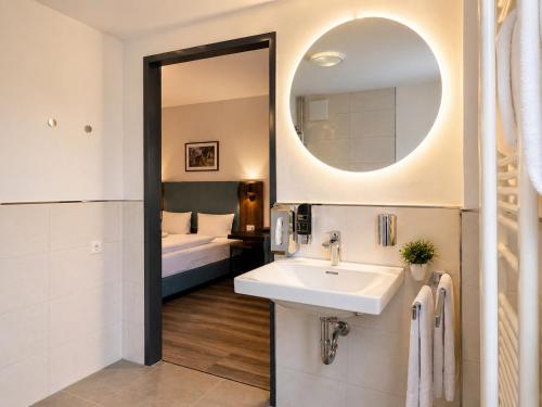 a bathroom with a sink and a mirror and a bed at Lillys Hotel München in Unterschleißheim