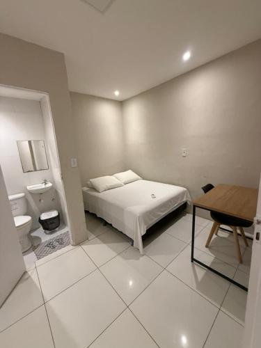 a white bedroom with a bed and a desk and a table at Pousada Meu Aconchego in Fortaleza