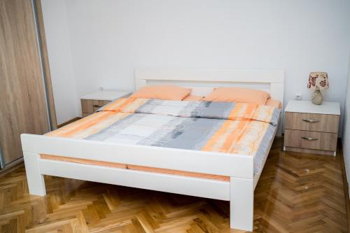 a white bed with an orange comforter in a bedroom at Apartman VITINA in Ljubuški