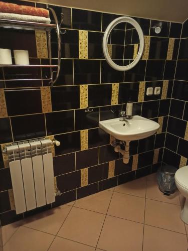 a black tiled bathroom with a sink and a mirror at Przylesie in Uniejow