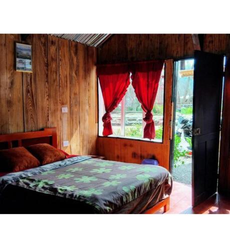 a bedroom with a bed and a window with red curtains at The Temple, Laguna de la Cocha in El Encano