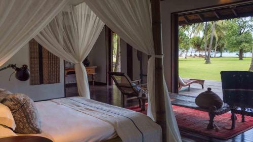 a bedroom with a canopy bed and a patio with a yard at Luxury Beachfront Villa in North Lombok in Gili Islands