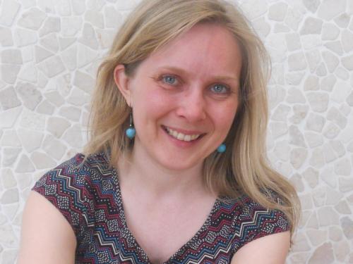 a woman with blonde hair and blue earrings smiles at the camera at Au Paradis Guesthouse in Waregem