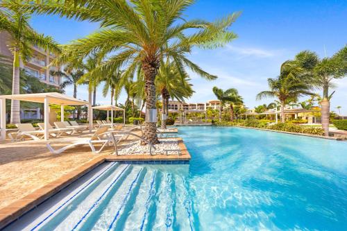 a pool at a resort with palm trees at Le Vent Eagle Beach Condos by Bocobay Aruba in Palm-Eagle Beach