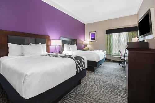 two beds in a hotel room with purple walls at La Quinta by Wyndham Pearland in Pearland