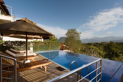 a swimming pool with an umbrella and benches next to at Villa Subashri, Victoria Golf Greens - Digana in Kandy