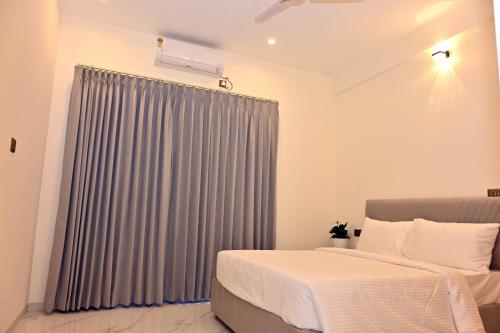 a bedroom with a bed and a gray curtain at Selora Suites Serviced Apartments in Mysore