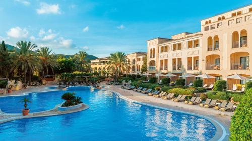 una piscina del complejo con sillas, palmeras y edificios en Steigenberger Hotel and Resort Camp de Mar, en Camp de Mar