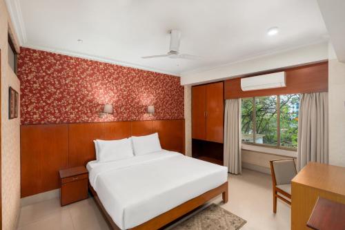a bedroom with a white bed and a desk and a window at The Classic Hotel in Imphal