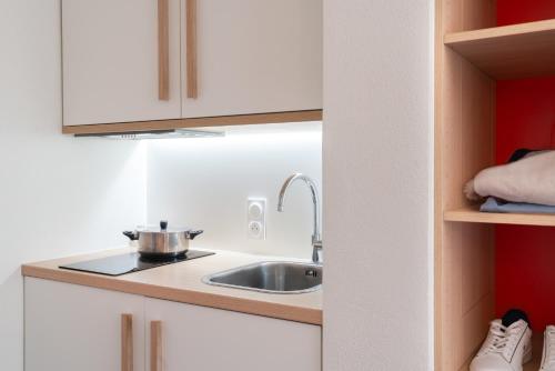 a kitchen with white cabinets and a sink at The Originals Residence Appart'Hôtel Lauréades Clermont-Ferrand Centre Jaude in Clermont-Ferrand