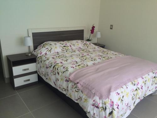 1 dormitorio con 1 cama y 2 mesitas de noche con colcha de flores en Departamento La Serena Laguna del Mar, en La Serena
