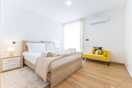 a white bedroom with a bed and a yellow chair at Dunes Beach House with Ocean Views in Viana do Castelo
