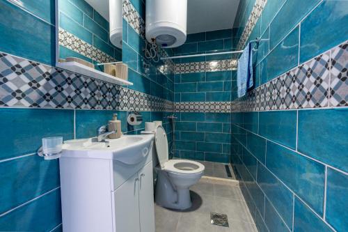 a blue tiled bathroom with a toilet and a sink at Benelux Apartments Bar in Šušanj