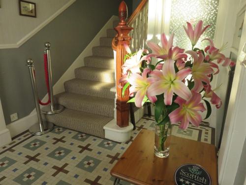 a vase of flowers on a table next to a staircase at Arduthie House in Stonehaven