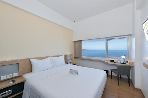 a bedroom with a bed and a desk and a window at Whiz Prime Hotel Megamas Manado in Manado