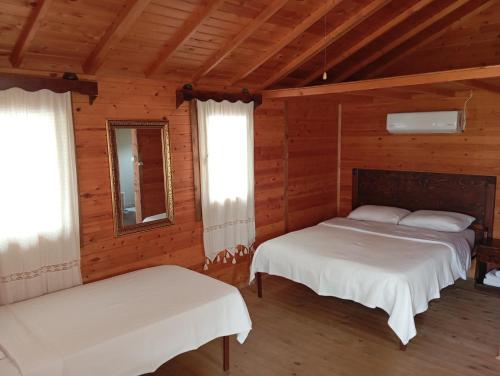 two beds in a room with wooden walls and windows at Fesleğenbükü Kamp in Çökertme