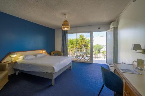 a bedroom with a bed and a desk and a balcony at Hotel AMERIQUE in Palavas-les-Flots