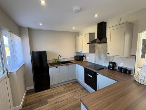 a kitchen with white cabinets and a black refrigerator at Ladysford Lets - The Duck in Peterhead