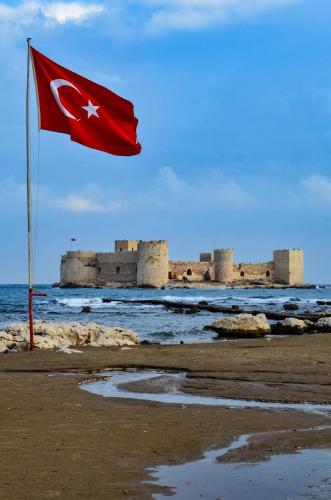 a flag on the beach with a castle in the background at Karsu apart otel in Erdemli